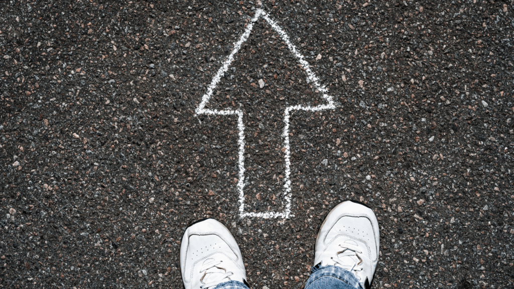 White sneakers standing on asphalt with a large white chalk arrow pointing forward.