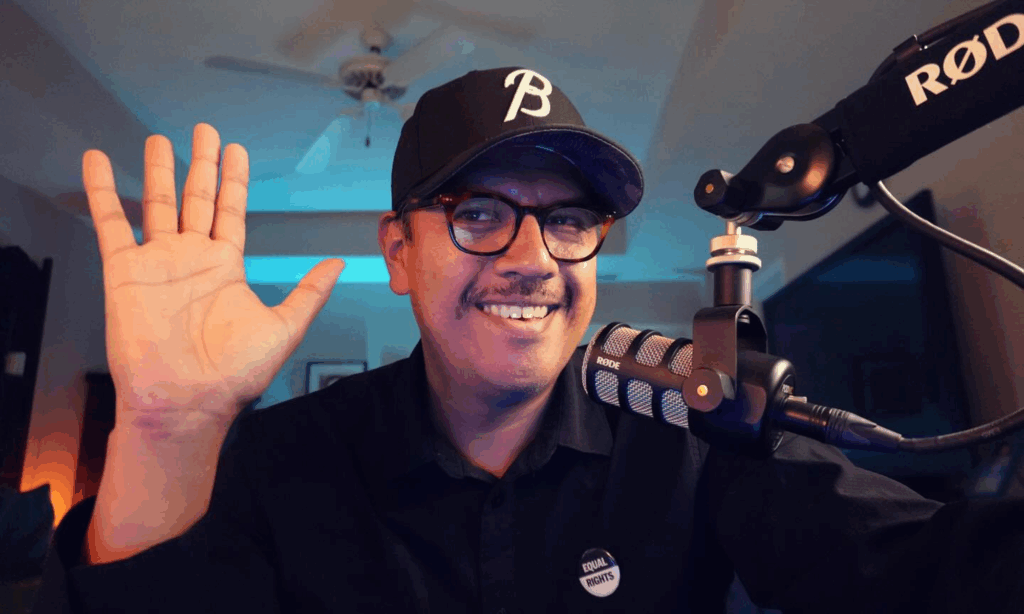 Tim Villegas in front of a Rode PodMic smiling and waving